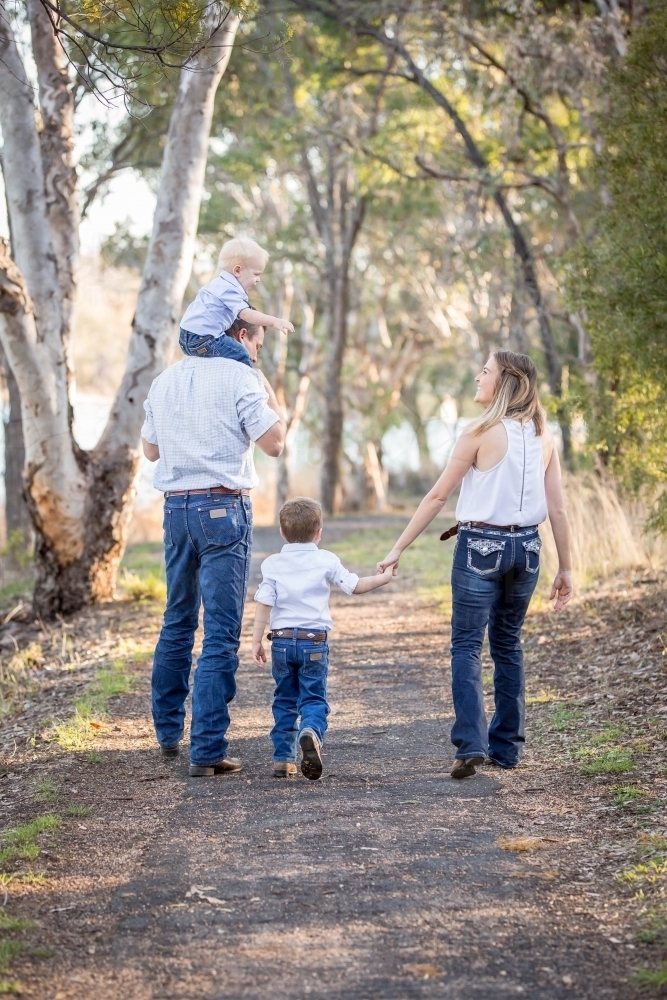 Father carrying young son on shoulders talking while mother holds son's hand - Australian Stock Image