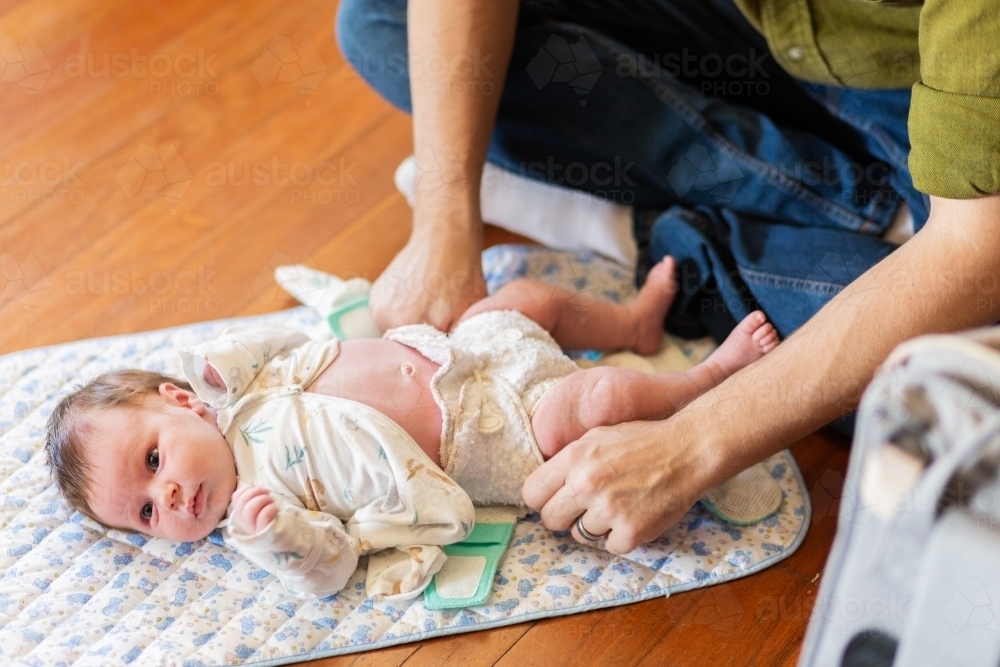 Father changing newborn baby's nappy on the floor - Australian Stock Image