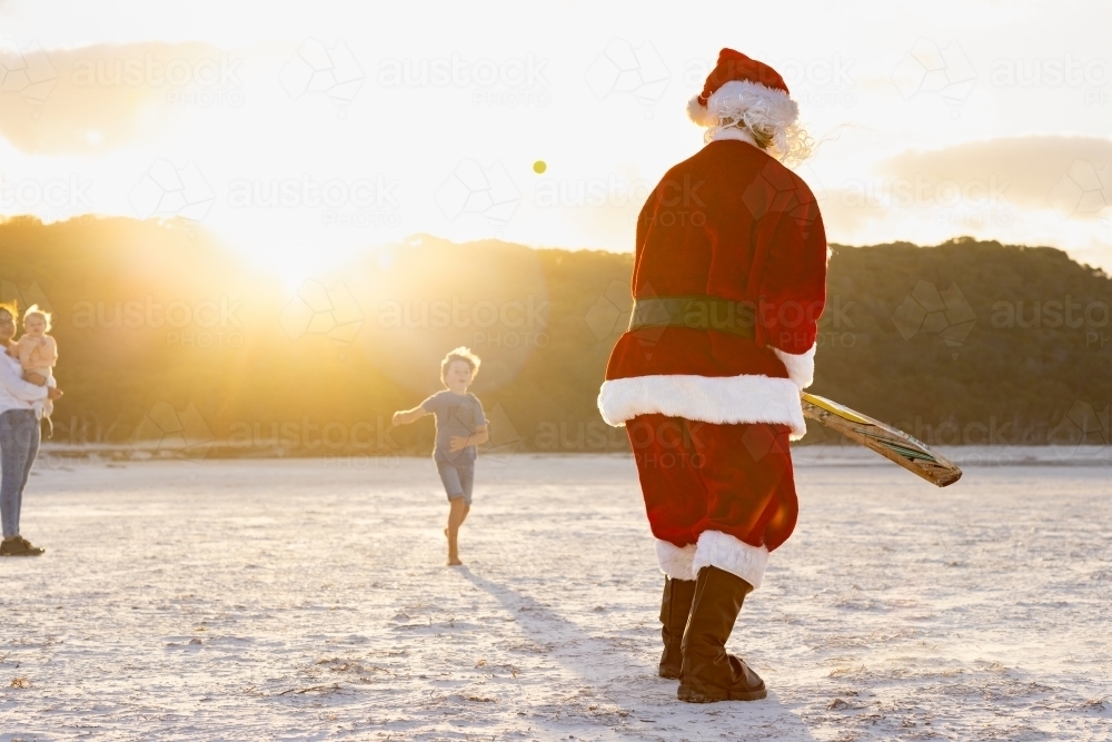 father christmas seen from behind facing a loose ball in beach cricket - Australian Stock Image