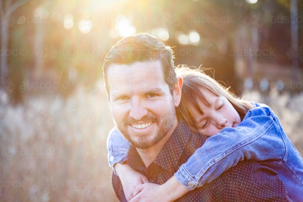 Father giving child a piggy back ride while she hugs him - Australian Stock Image