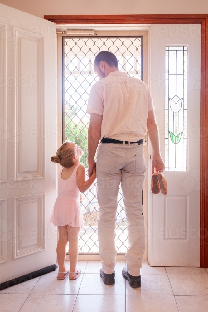 Father holding daughters hand walking out front door to ballet lesson - Australian Stock Image