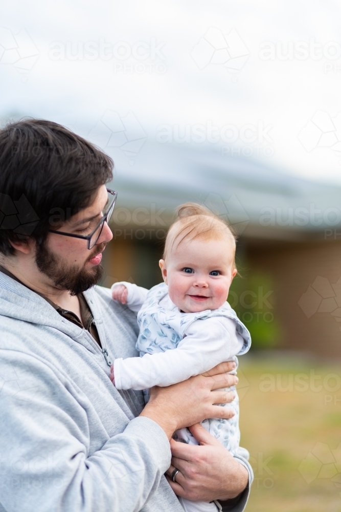 father holding happy five month old baby outside on winter walk - Australian Stock Image
