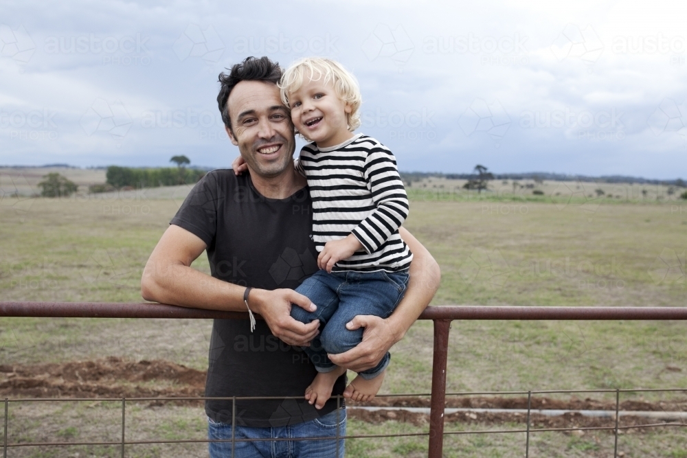 Father holding happy young son on an old farm fence - Australian Stock Image