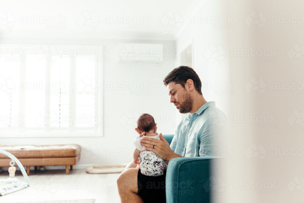 Father holding newborn baby upright in the living room. - Australian Stock Image