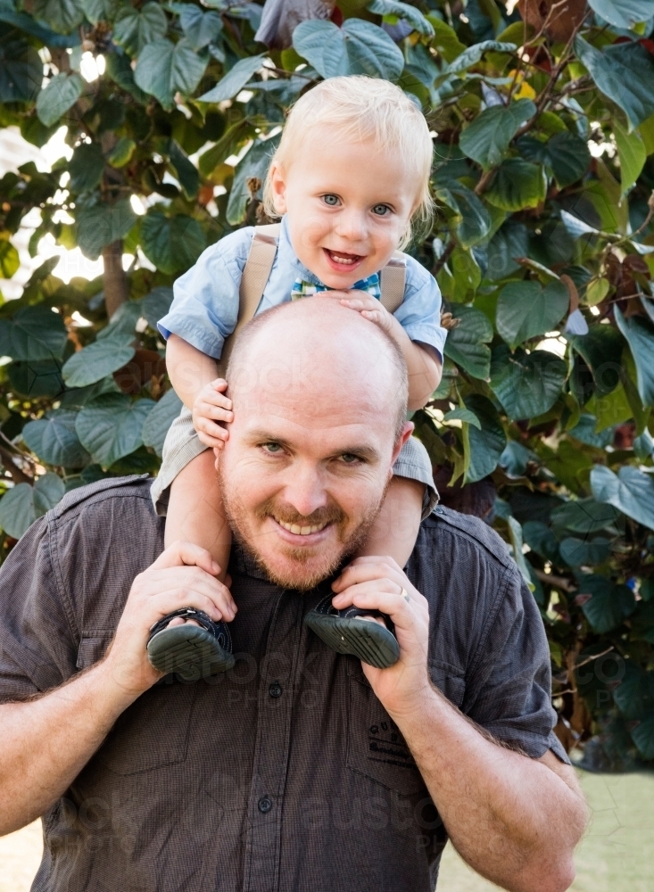 Father holding son on shoulders while smiling at the camera. : Austockphoto Father holding son on shoulders while smiling at the camera. - Australian Stock Image