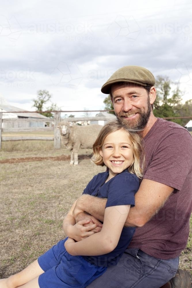 Father hugging daughter on farm with sheep in background - Australian Stock Image