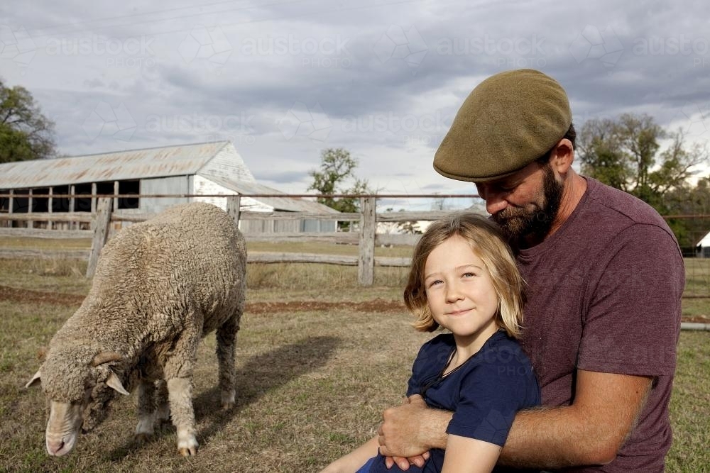 Father hugging daughter outside with sheep in paddock - Australian Stock Image