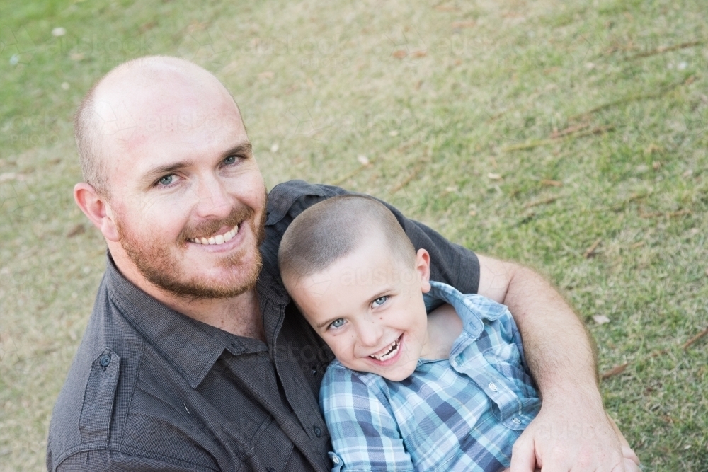 Father hugging son while smiling at the camera. - Australian Stock Image