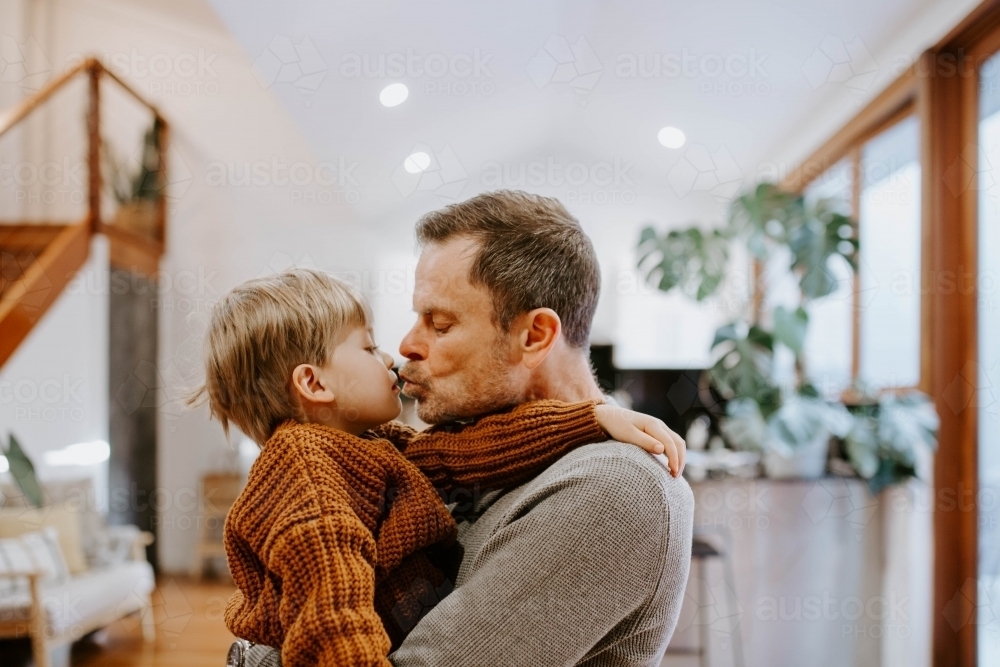 Father kissing young son inside home - Australian Stock Image
