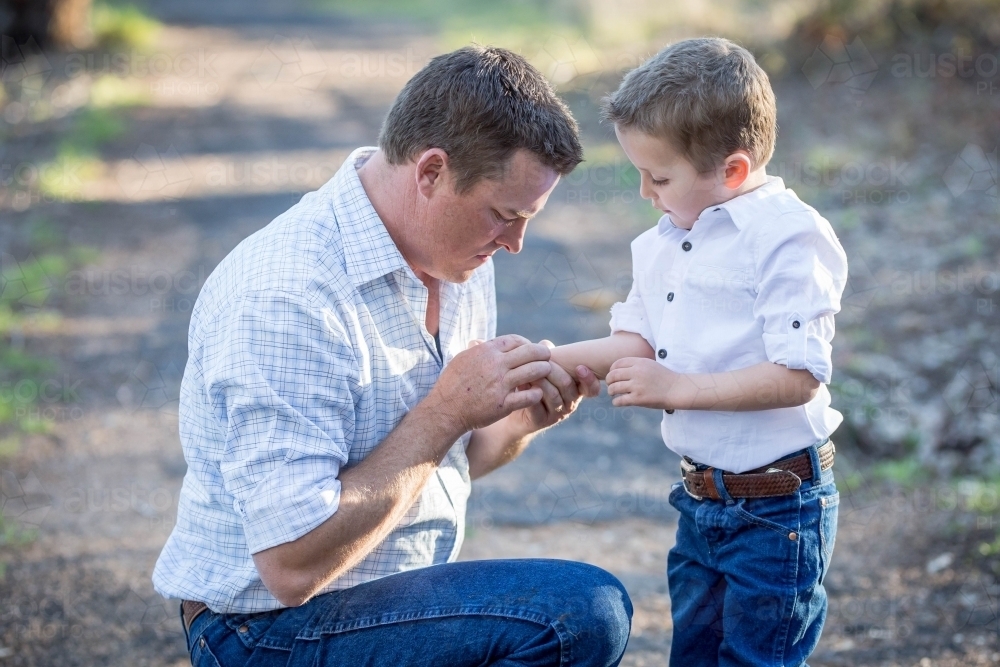 Father kneeling down to care for scrape on son's arm - Australian Stock Image