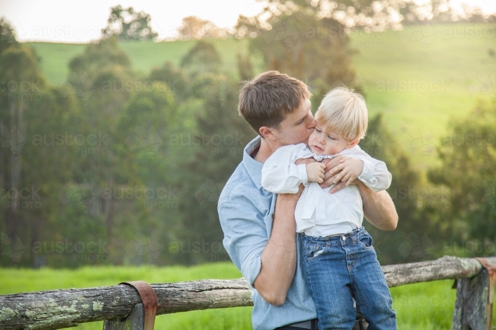 Father lifting son up to kiss him outside on farm - Australian Stock Image