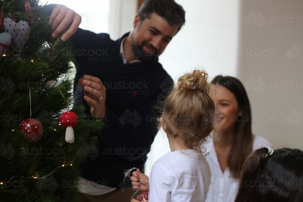 Father, mother and daughter decorating Christmas tree - Australian Stock Image