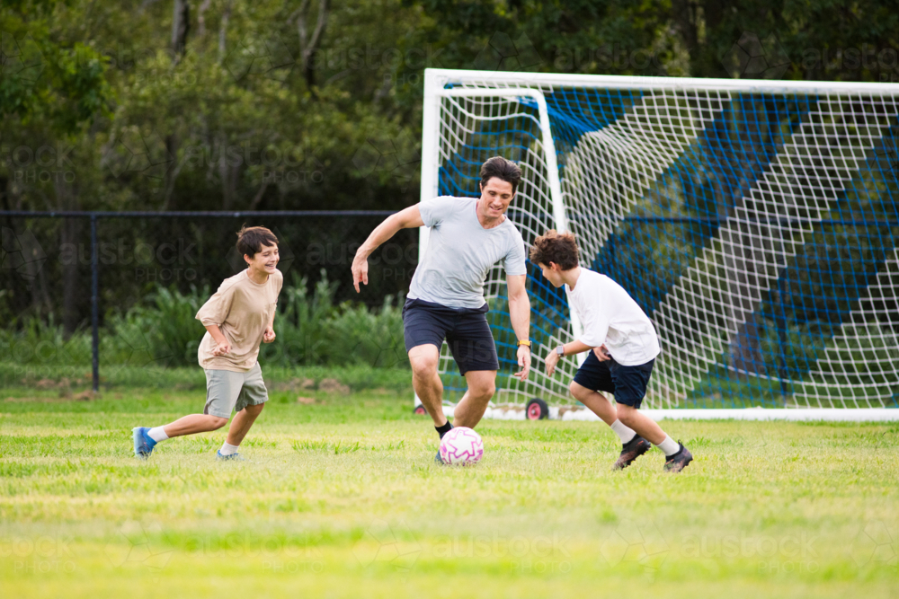Father playing soccer with his sons on green soccer field - Australian Stock Image