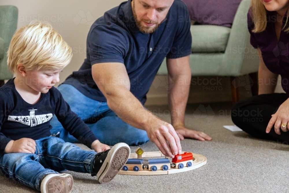 Father playing with son and toy train on floor of speech clinic - Australian Stock Image