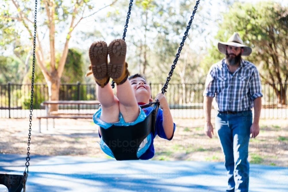 Father pushing son on the swing at the park - Australian Stock Image