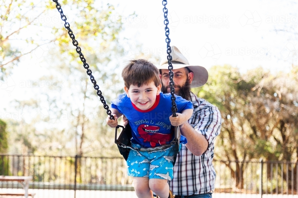 Father pushing son on the swing at the park - Australian Stock Image