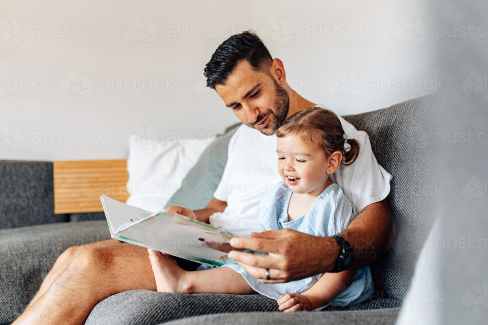 Father reading story with toddler daughter on the couch - Australian Stock Image