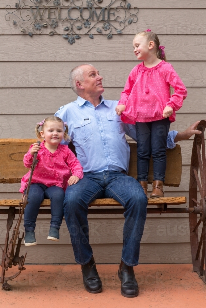 Father sitting on a bench with his two young daughters - Australian Stock Image