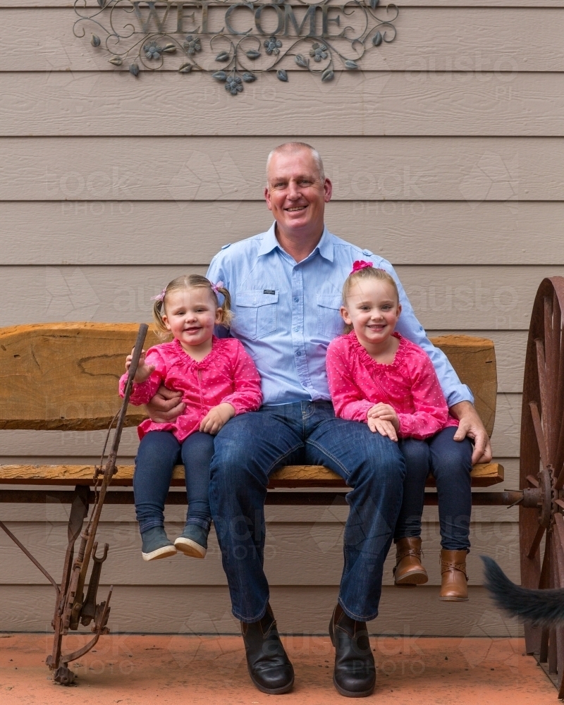 Father sitting on a bench with his two young daughters - Australian Stock Image