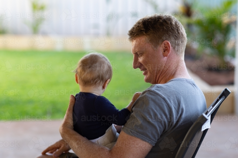 Father sitting on patio holding baby wearing a hip brace - Australian Stock Image