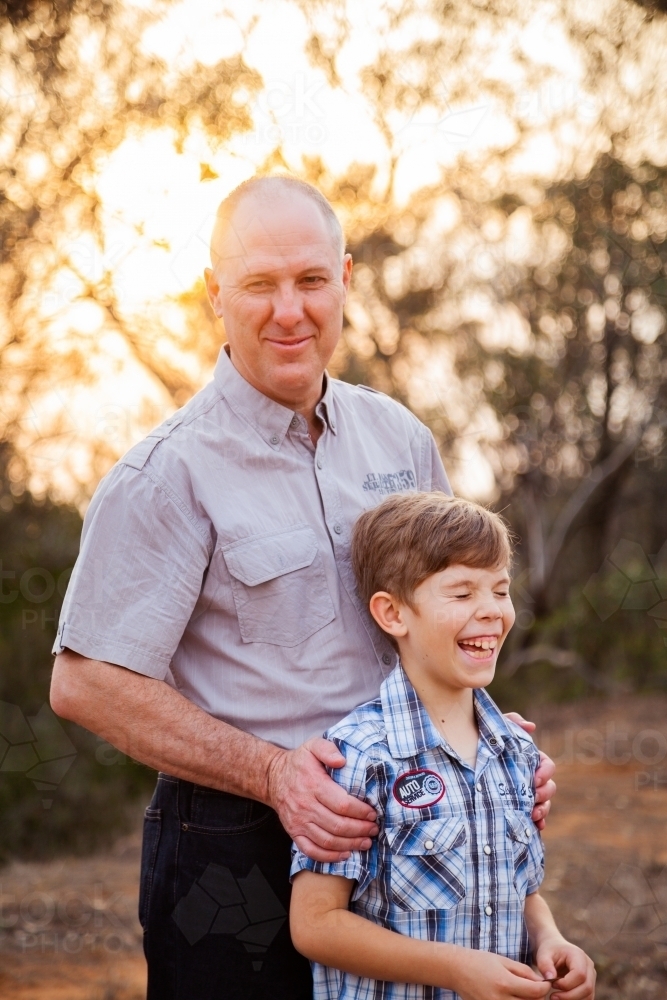 Father smiling and son laughing in orange sunset light - Australian Stock Image