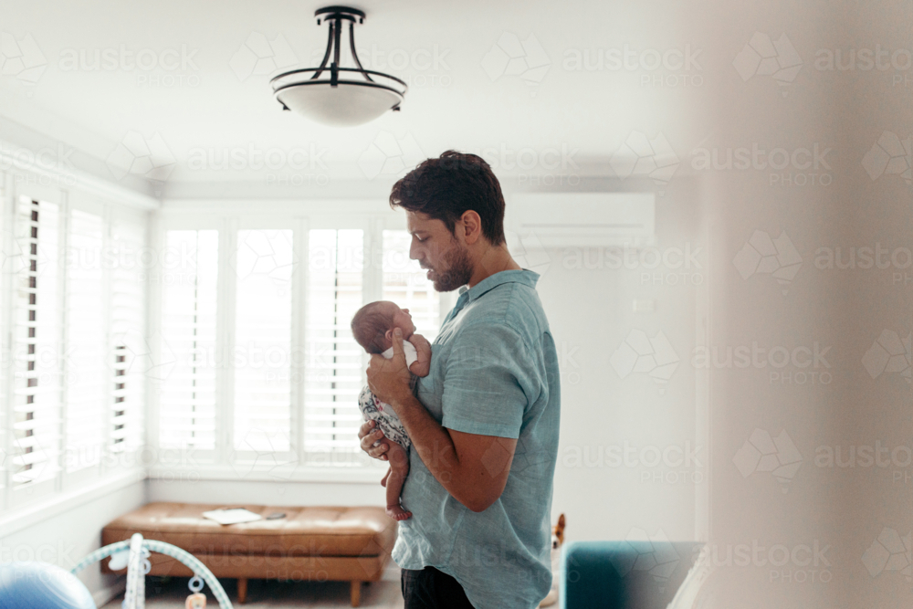 Father standing holding newborn baby upright in the living room - Australian Stock Image