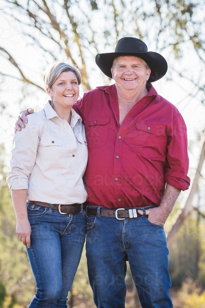 Father standing with arm around daughter on family farm property wearing akubra smiling - Australian Stock Image