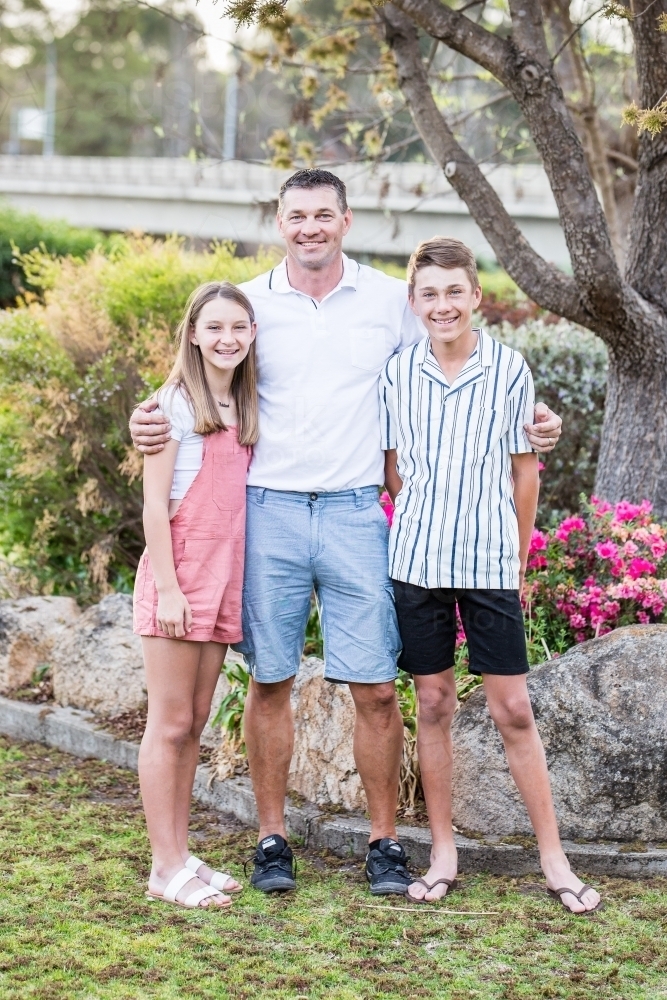 Father standing with arms wrapped around children happy - Australian Stock Image