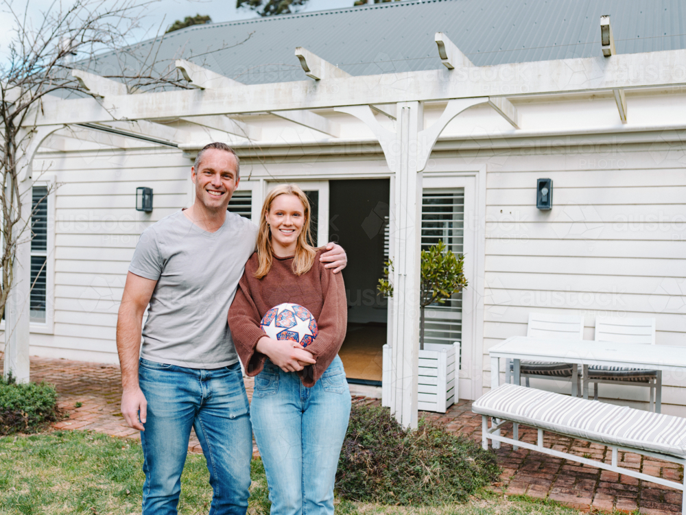 Father stands close with teenage daughter with his arms over her shoulder - Australian Stock Image
