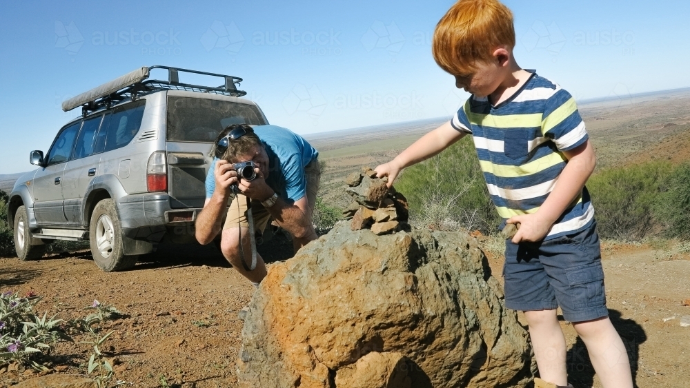 Father taking a photo of his young son making a rock tower in the outback - Australian Stock Image