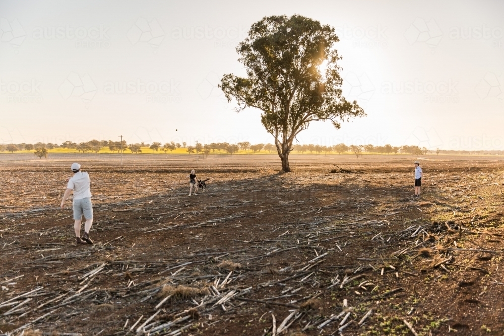 Father throwing ball with children in dirt paddock on farm - Australian Stock Image