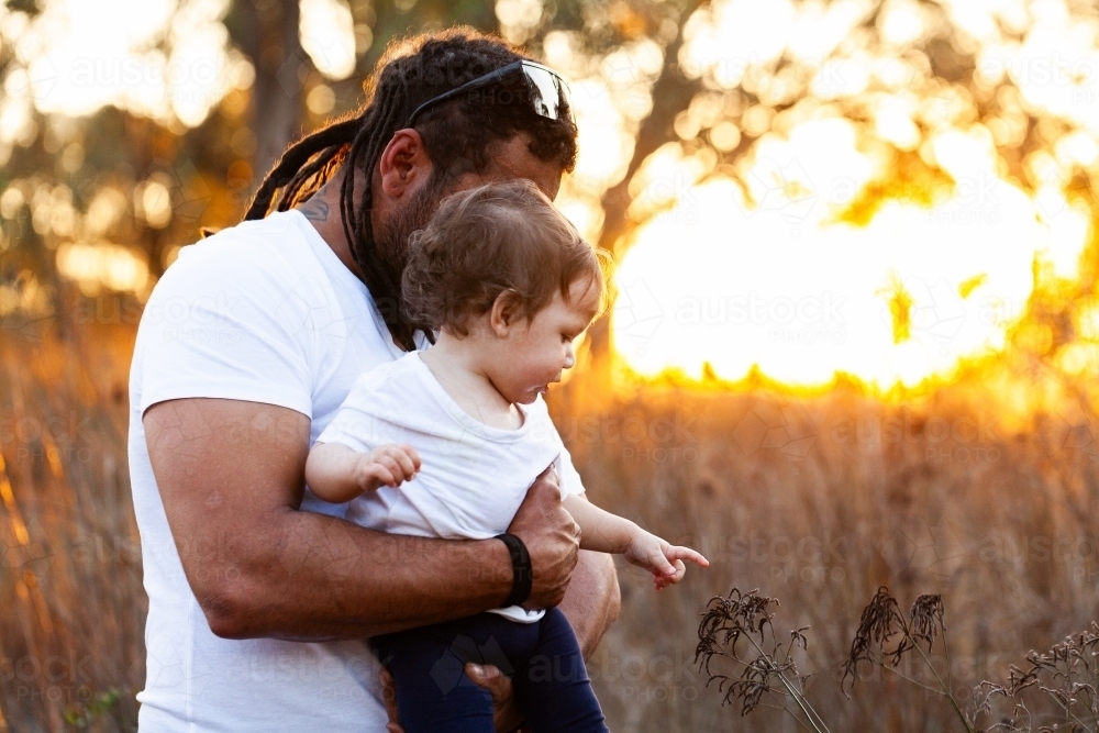 Father with baby daughter showing her plants in nature at sunset - Australian Stock Image