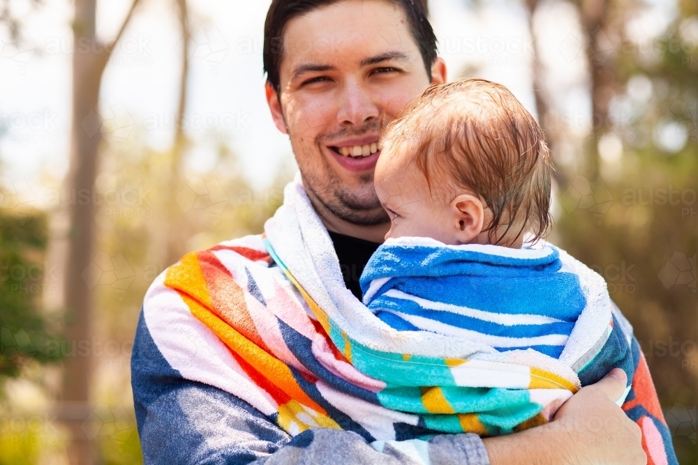 Image of Father with baby wrapped up in towel after swimming in pool in