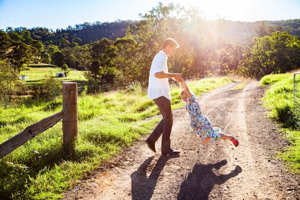 Father with daughter spinning outside on farm driveway - Australian Stock Image