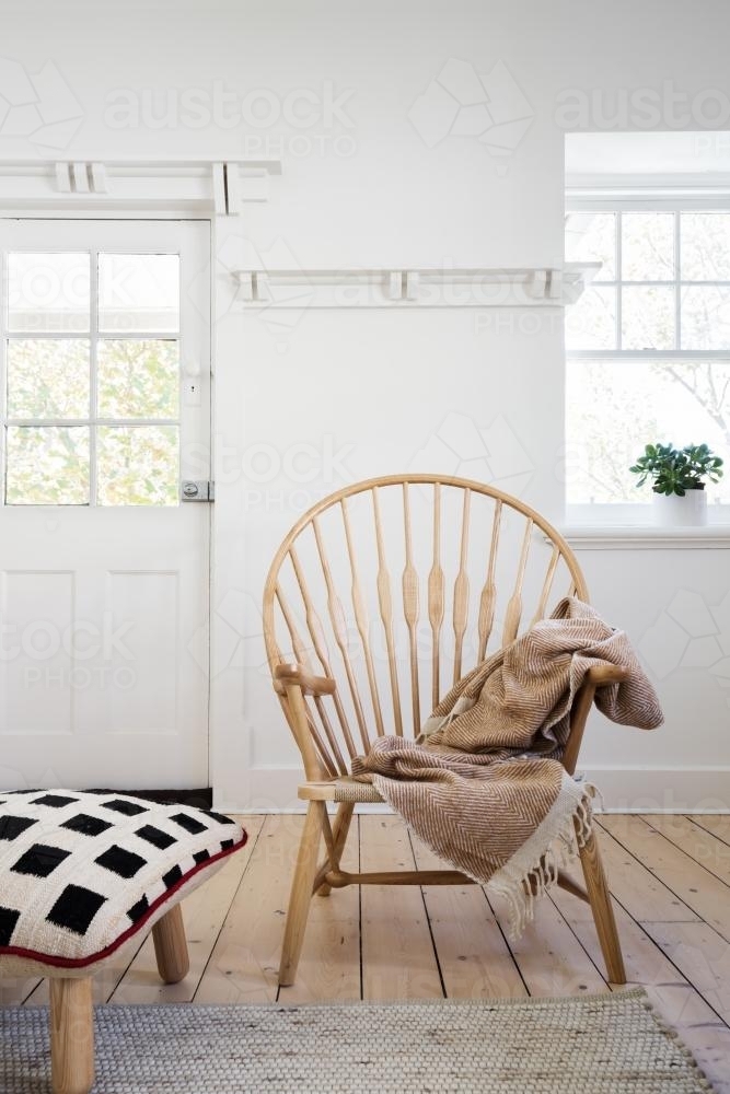 Feature wooden arm chair with throw and cushion ottoman in modern designer apartment - Australian Stock Image