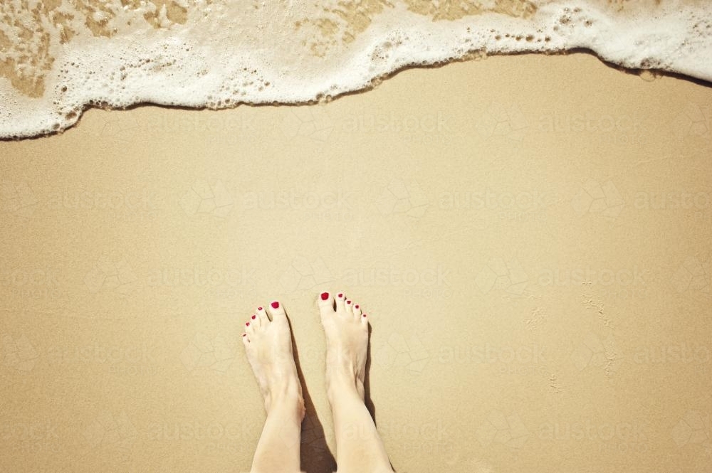 Feet on the sand as a wave approaches - Australian Stock Image