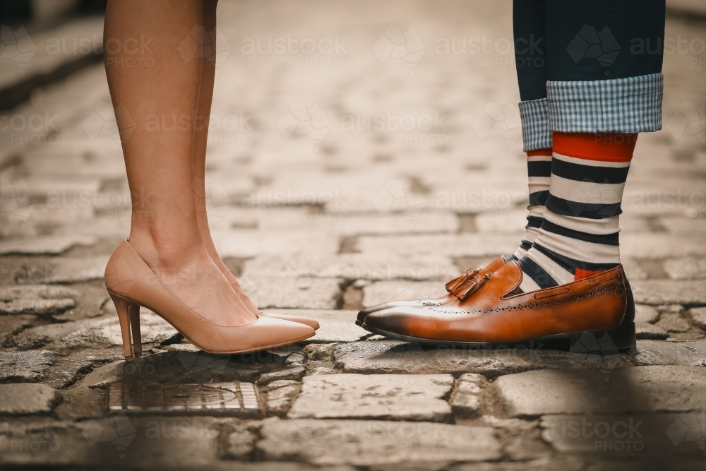 Feet only shot of couple standing together on cobblestone lane - Australian Stock Image