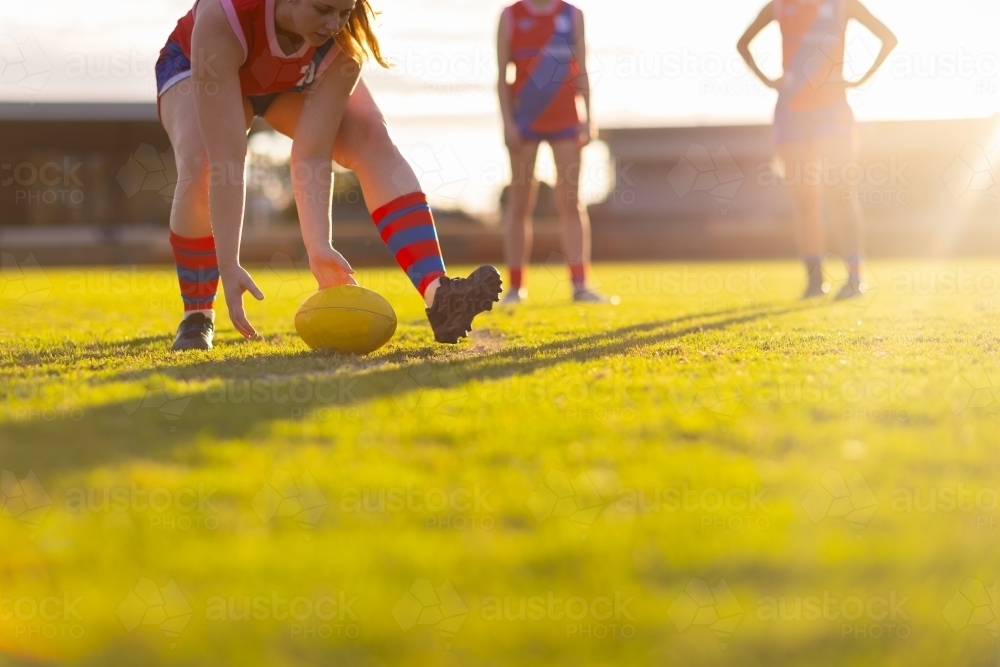 female aussie rules footballer bending to scoop up ball - Australian Stock Image