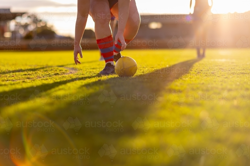 female aussie rules footballer bending to scoop up ball - Australian Stock Image