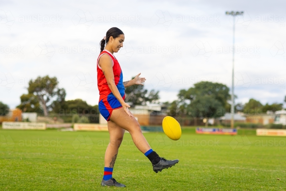 female Australian rules football player kicking ball - Australian Stock Image