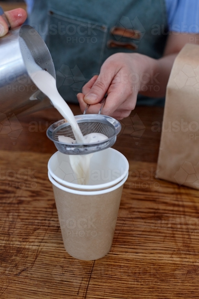 Female barista pouring milk chai drink into cup on a cafe benchtop - Australian Stock Image
