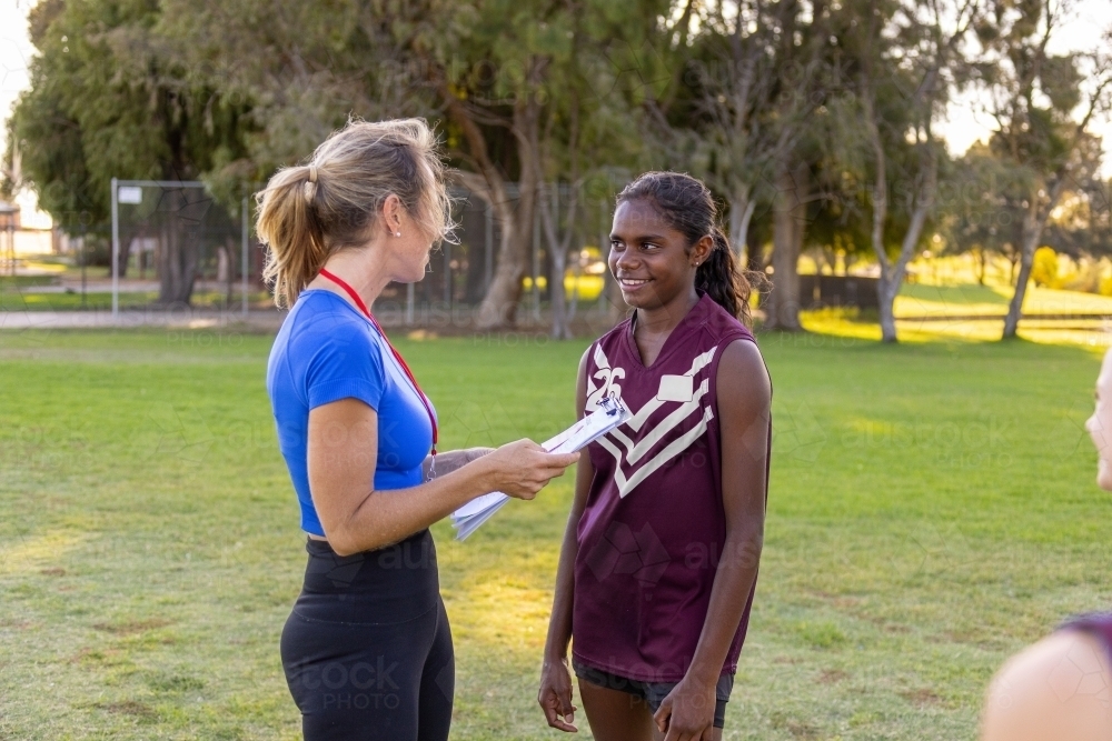 female coach talking to aboriginal girl on football field - Australian Stock Image