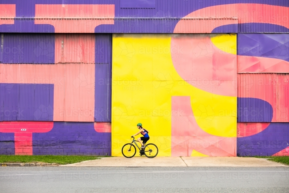 Female cyclist in front of bright coloured wall - Australian Stock Image