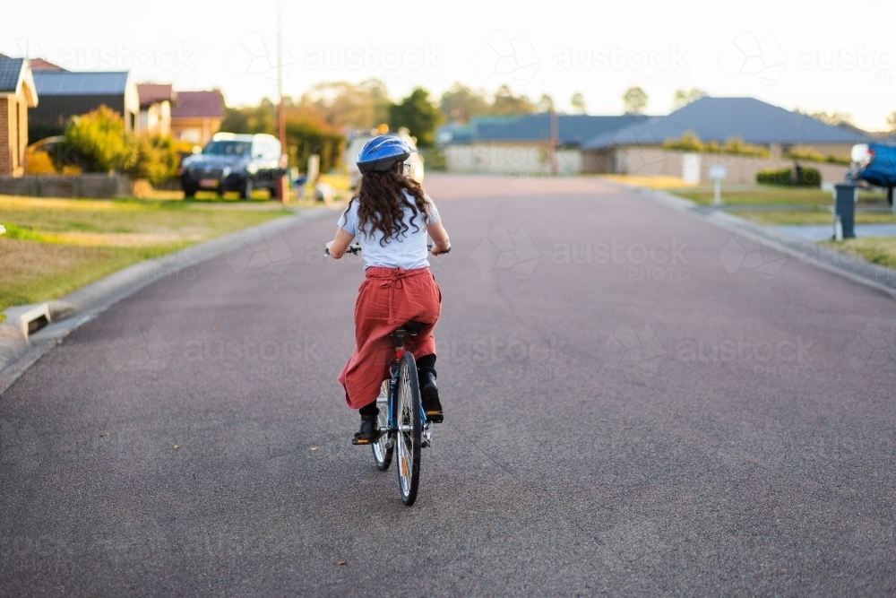 Image of female cyclist riding away up suburban road with copy space ...