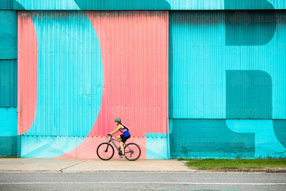 Female Cyclist Riding by a Colourful Wall - Australian Stock Image