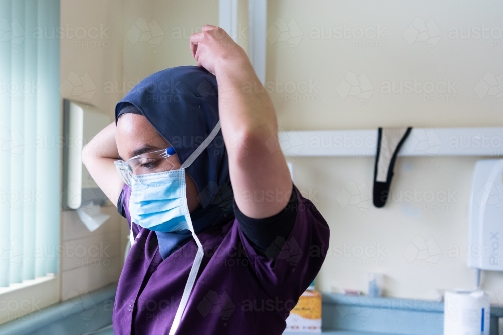 Female dentist wearing hajib putting on surgical mask - Australian Stock Image