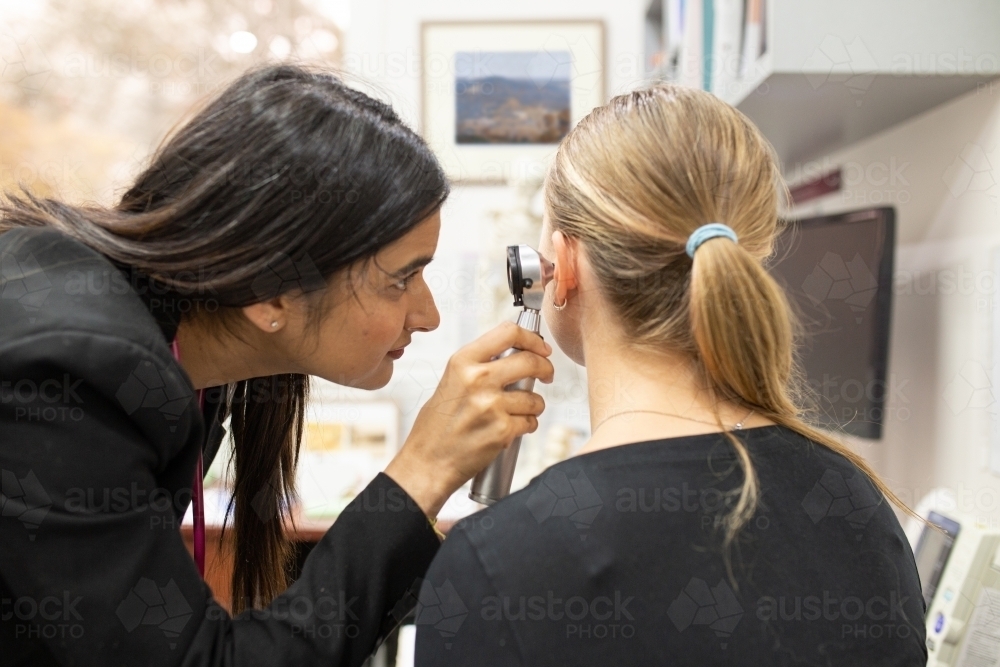 female doctor checking the woman's ear with an otoscope in a clinic - Australian Stock Image