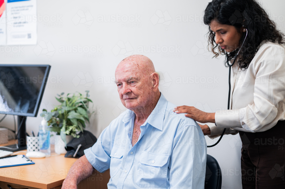 Female doctor listens to elderly mans back using a stethoscope during a routine check‑up - Australian Stock Image