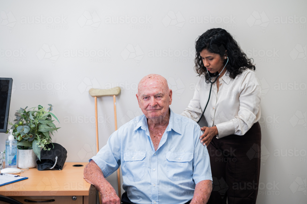 Female doctor listens to elderly mans back using a stethoscope during a routine check‑up - Australian Stock Image