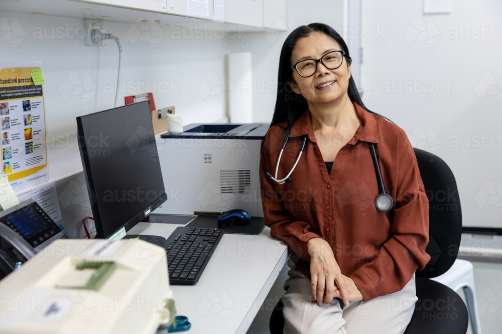 Female doctor sitting behind her desk inside exam room - Australian Stock Image